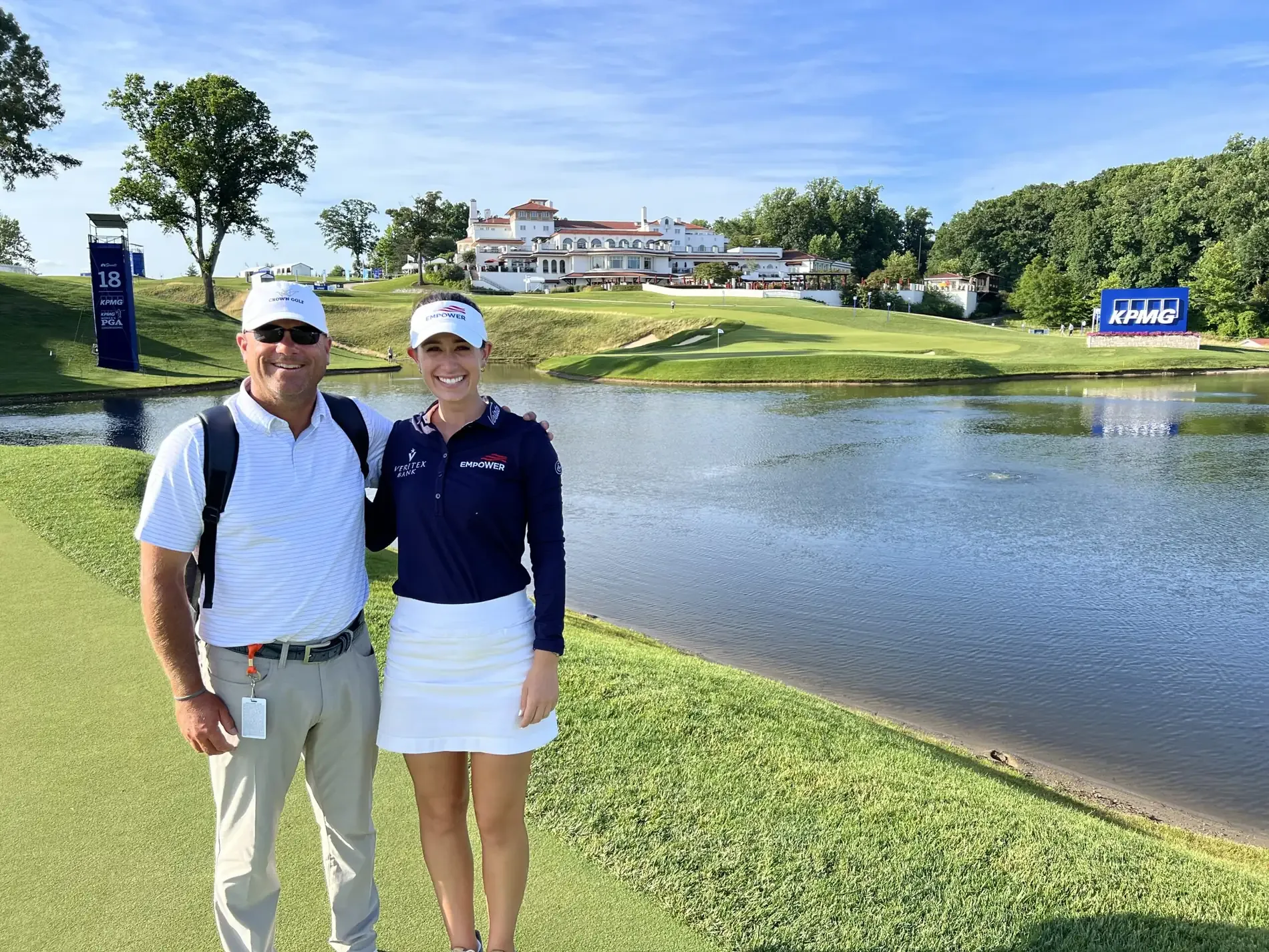 Joey Wuertemberger and LPGA player Cheyenne Knight smiling beside a pond, with a large clubhouse across the water