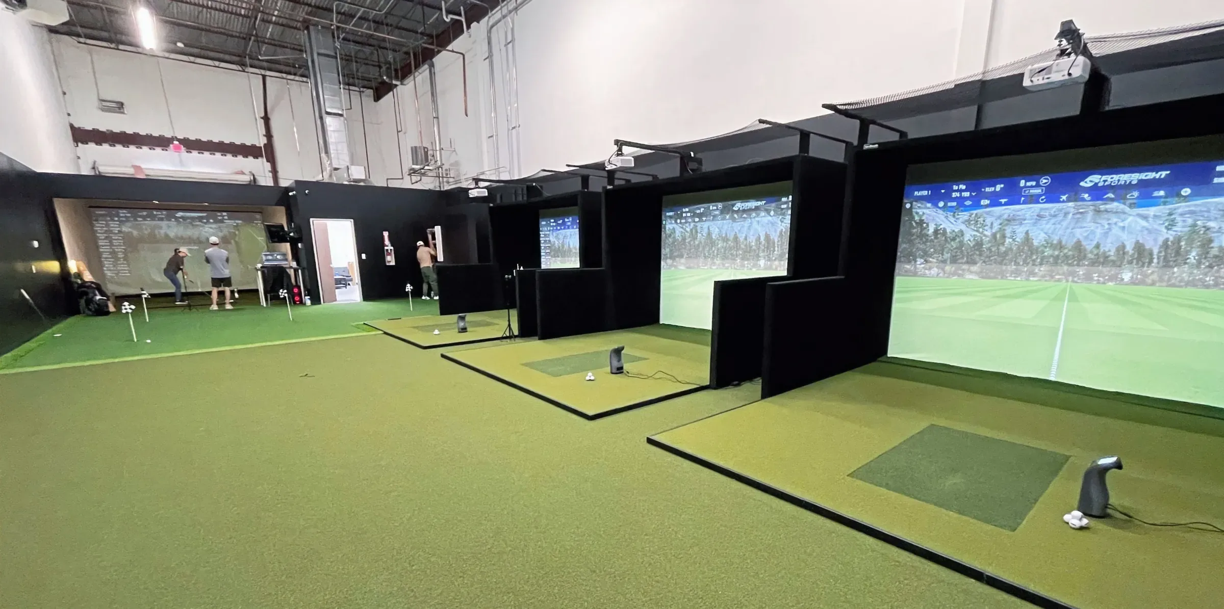 Row of indoor golf simulator bays with projector screens and turf hitting mats at Texas Golf Studio, Houston