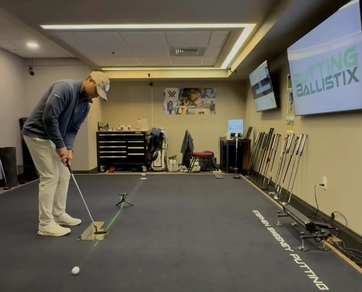 Golfer putting on an indoor putting studio mat with camera tracking equipment and wall screens in Madison