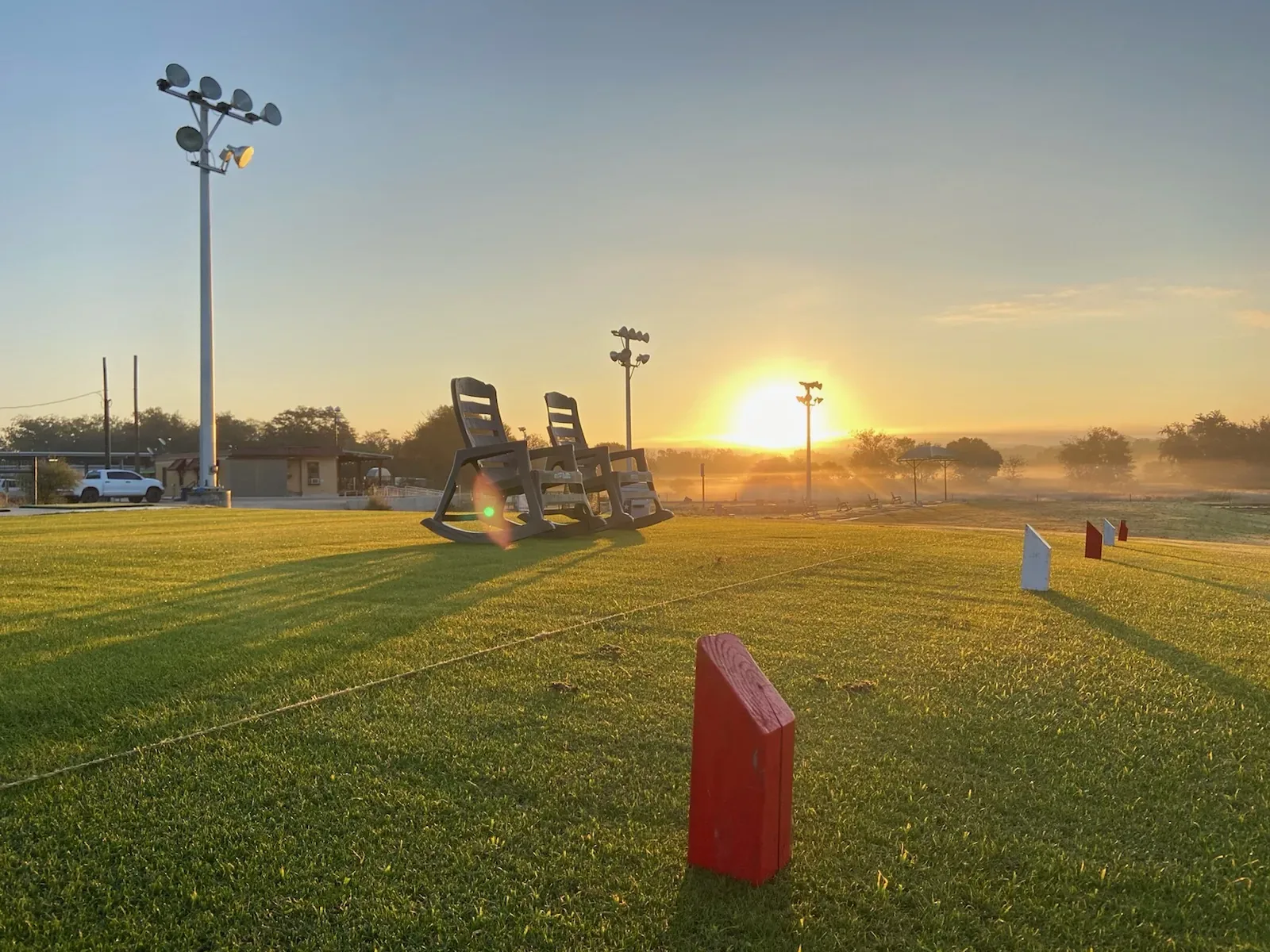 Sunrise over the practice tee with rocking chairs, floodlight poles and a red tee marker at David Ogrin Golf Academy