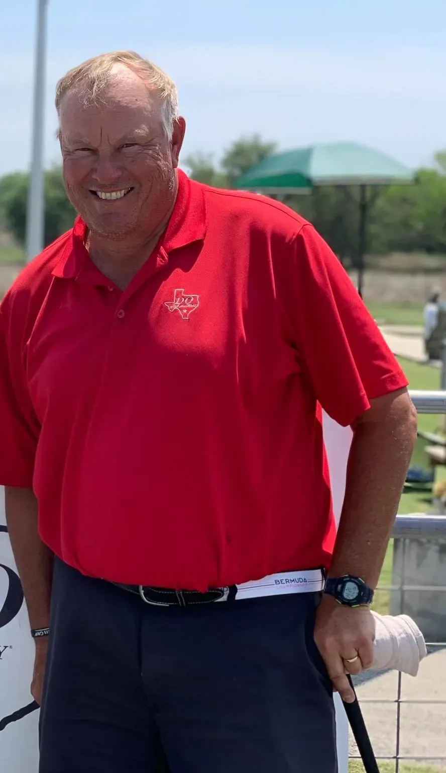 David Ogrin smiling in a red academy polo shirt, standing beside a banner at a driving range