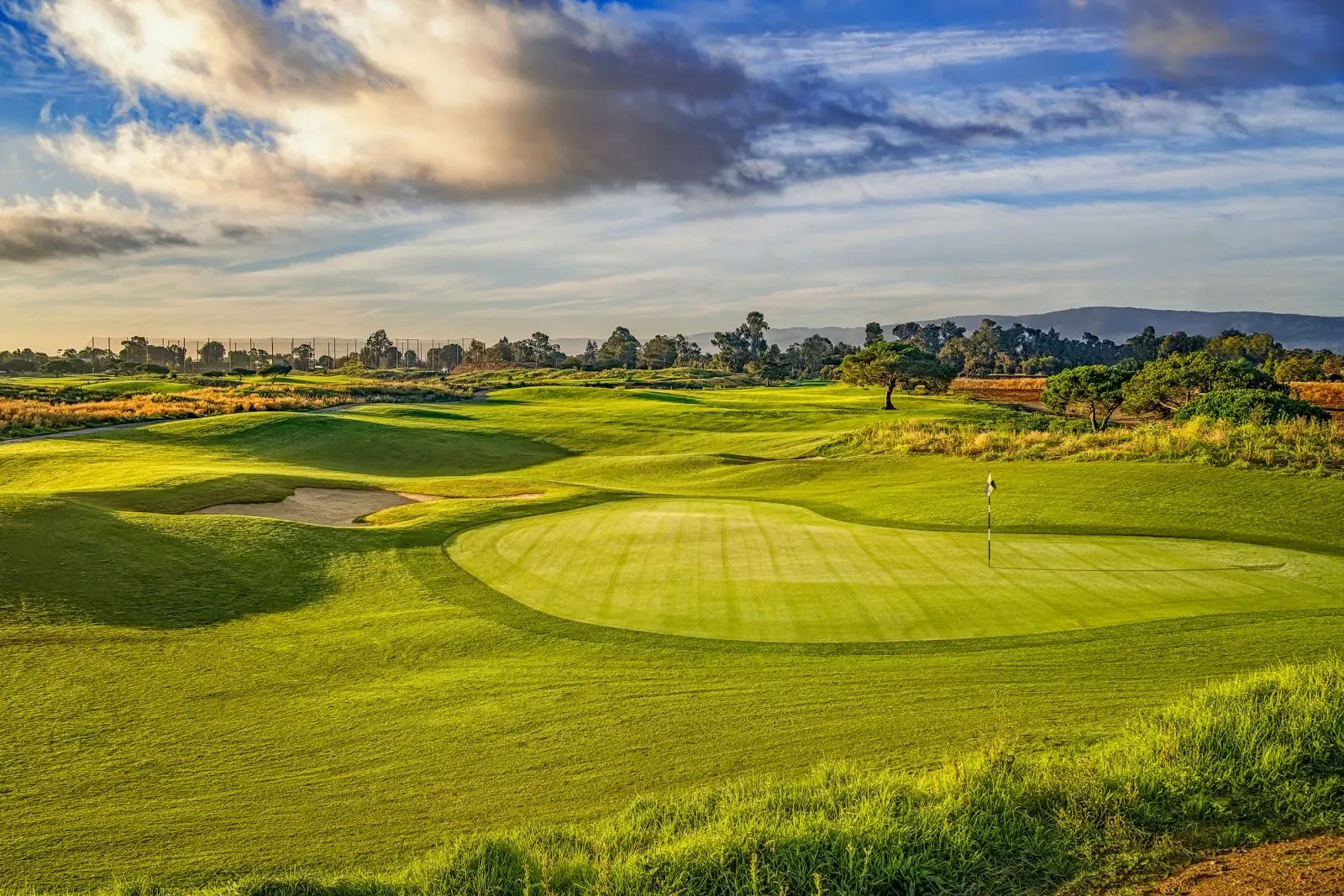 Sunlit green and bunker with mowing stripes and distant hills at Baylands Golf Links, Palo Alto.