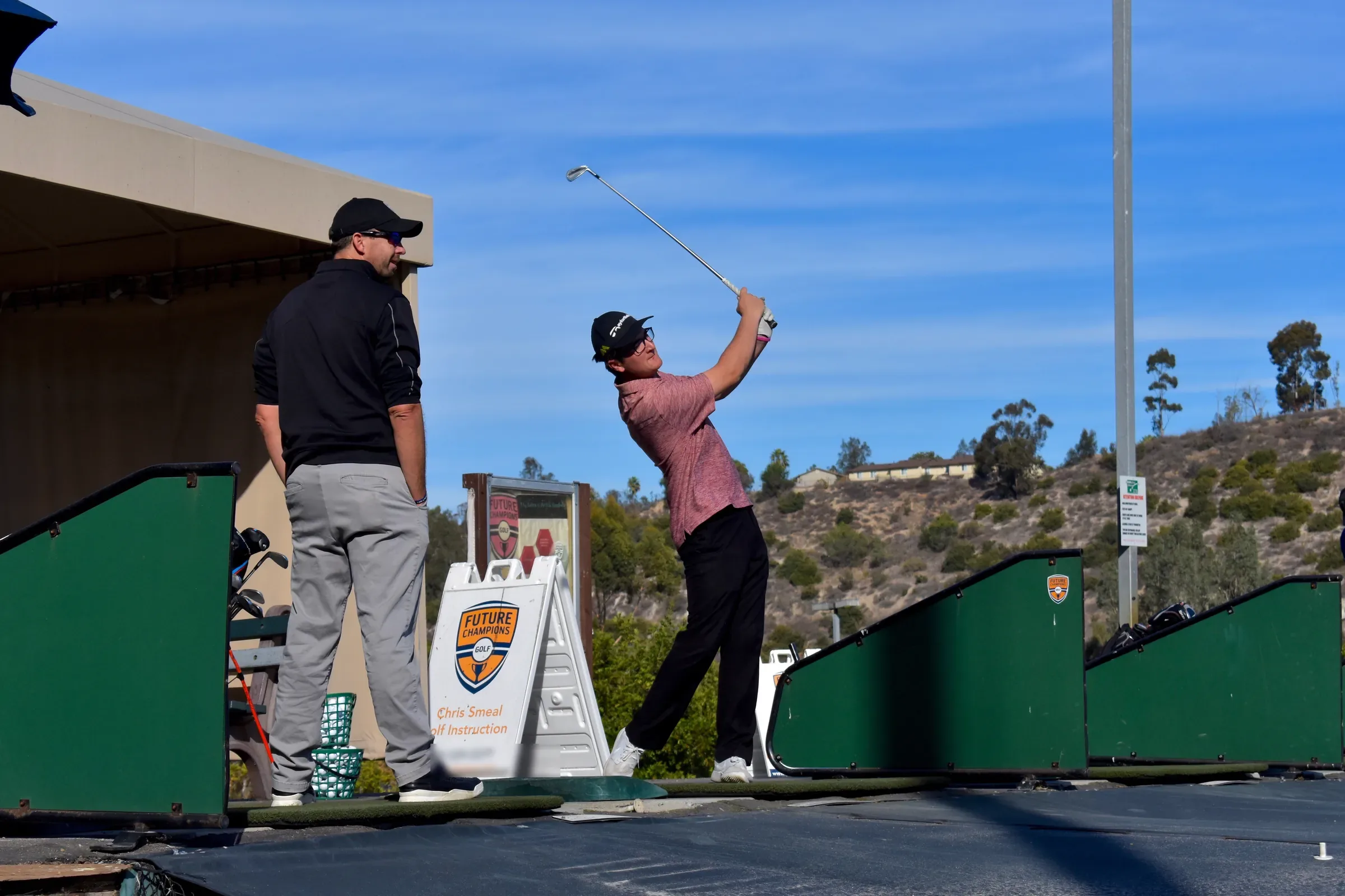 A coach watches a golfer finish an iron swing at the hitting bays of the driving range, Future Champions Golf in San Diego.