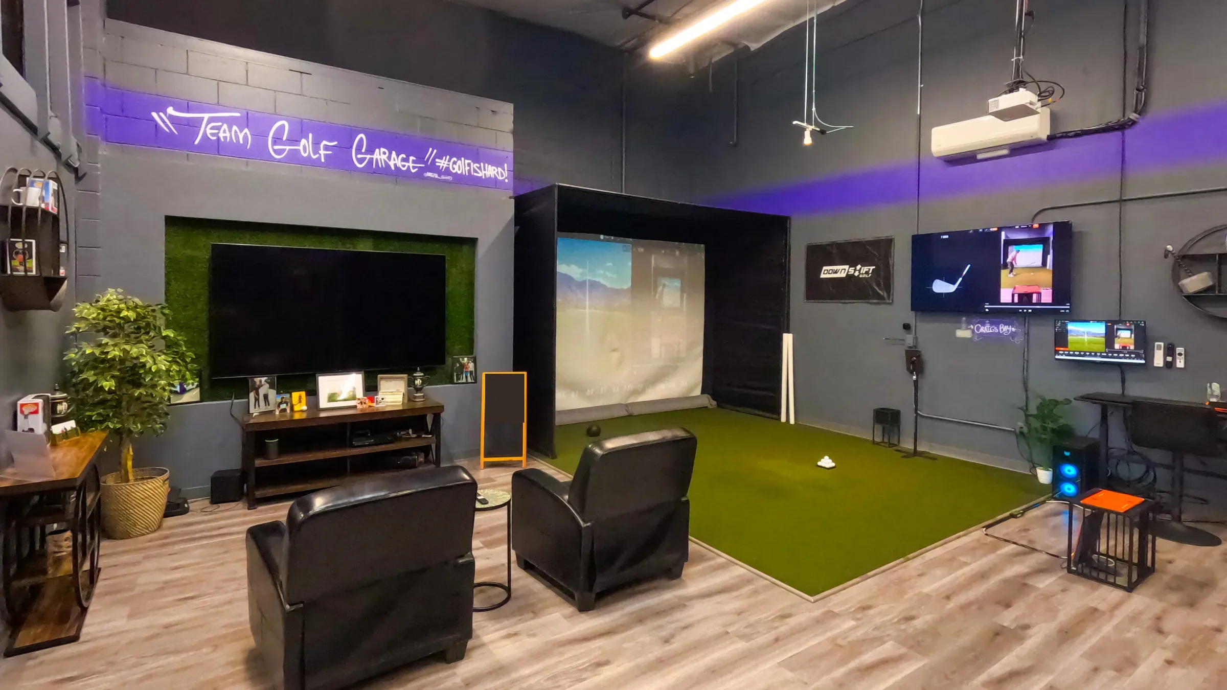Lounge chairs and a wall TV facing the hitting bay and screen inside The Golf Garage in San Jose.